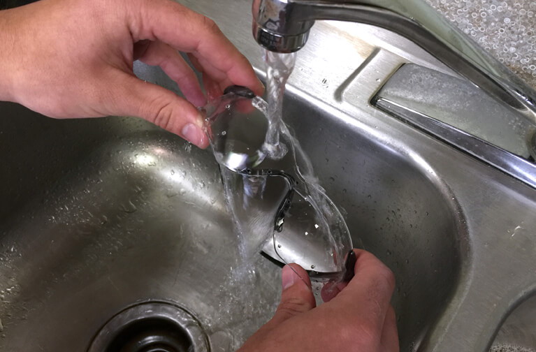 Hình ảnh một đôi bàn tay đang cầm một cặp kính và rửa dưới vòi nước